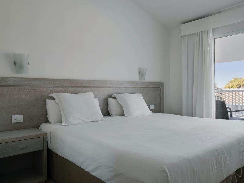 Een eenvoudige hotelkamer met een groot tweepersoonsbed en balkonuitzicht.