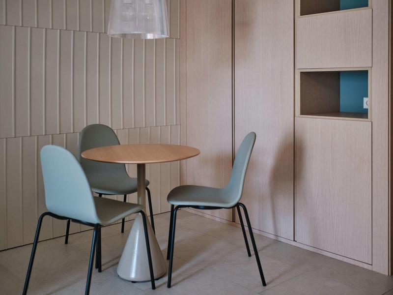 Moderne zithoek met ronde houten tafel en vier blauwe stoelen tegen een beige muur