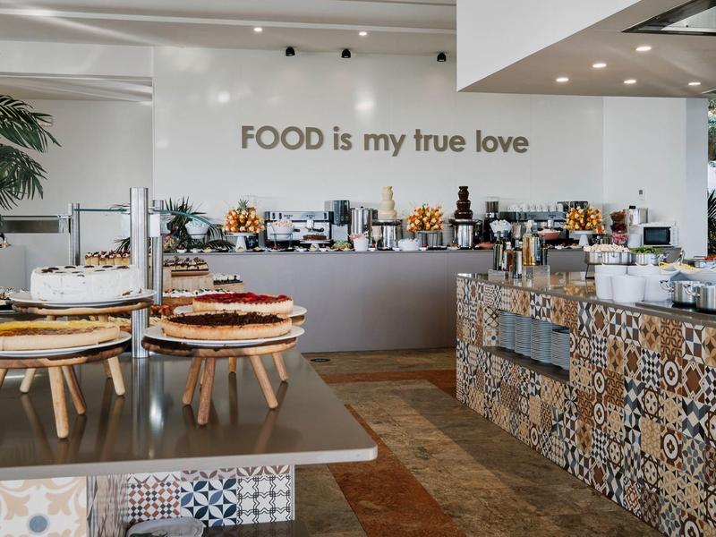 Modern zelfbedieningsrestaurant met taarten en koffie, decoratief betegeld en helder verlicht.