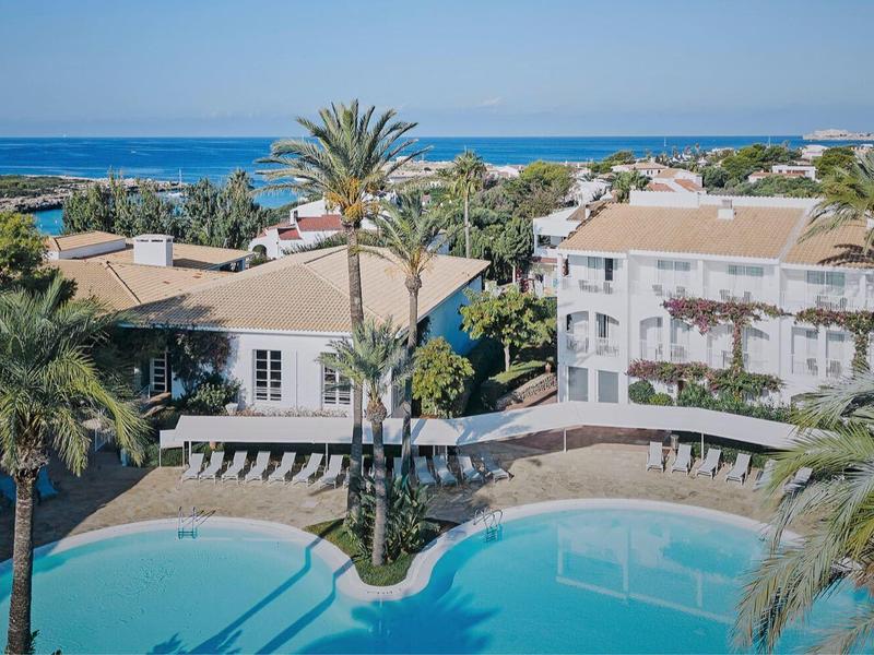 Hotelcomplex met twee grote zwembaden, omgeven door palmbomen en uitzicht op de blauwe zee.
