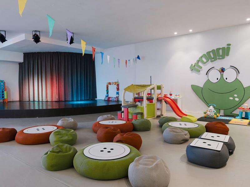 Lichte kinderruimte met kleurrijke kussens en een kleine glijbaan voor een podium.