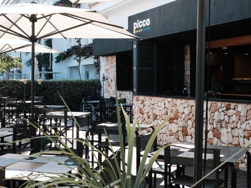 Buitengebied van een café met tafels, stoelen en grote witte parasols bij daglicht.