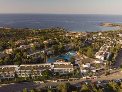 Aerial view of a resort with pool, surrounded by greenery and overlooking the sea