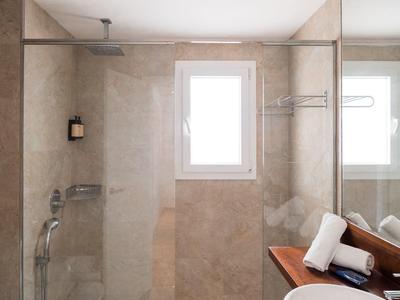 Modern bathroom with walk-in shower, sink, and towels on wooden shelf.