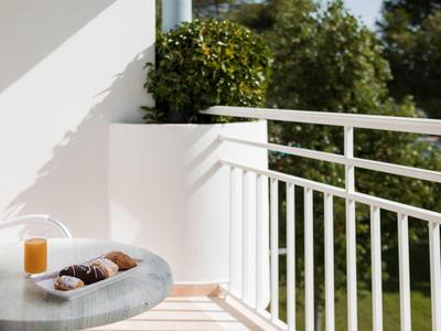 Balcony with modern railing, table with juice and pastries, green trees in the background