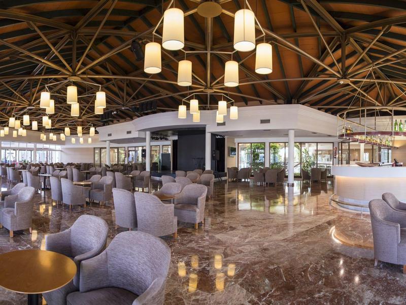 Large, elegant hotel lounge area with round tables, chairs, and modern hanging lights.