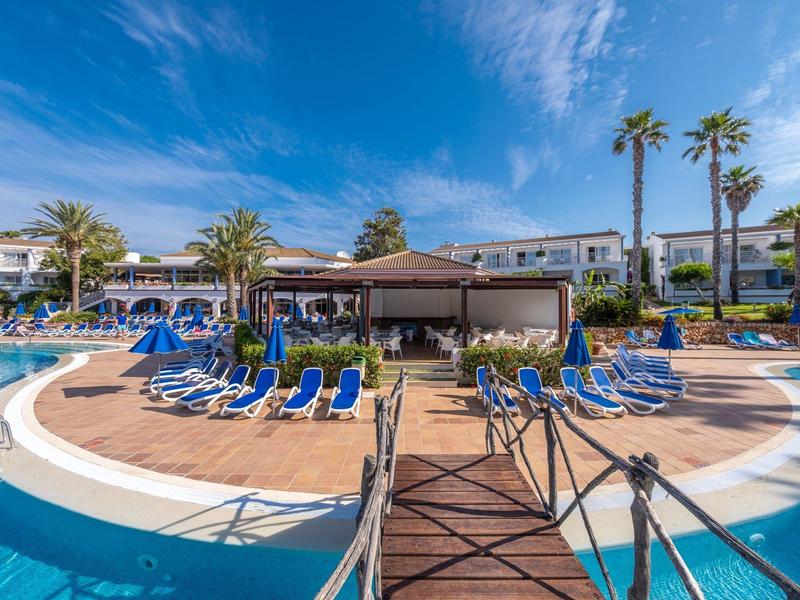Hotel pool with blue lounge chairs and palm trees under a blue sky