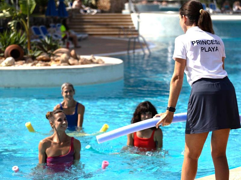 Woman demonstrating swimming exercise with pool noodle in hotel pool.