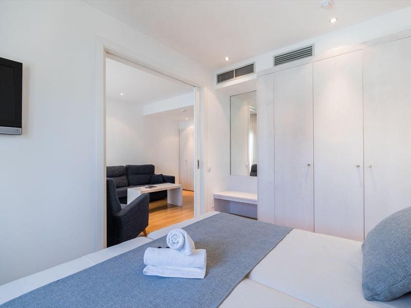 Modern hotel room with bed, TV, closet, and adjoining living room with sofa.