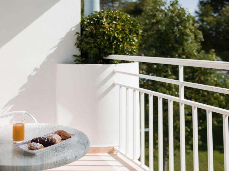 Balcony with modern railing, table with juice and pastries, green trees in the background