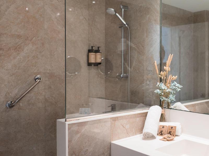 Elegant bathroom with marble walls, glass shower, and decorative flower arrangement.