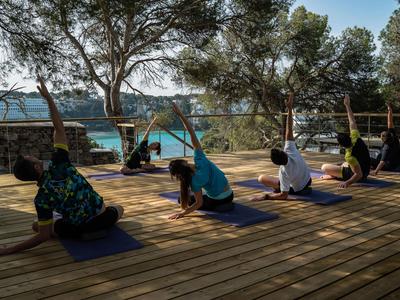 Menschen praktizieren Yoga auf einer Holzterrasse mit Blick auf das Meer und Bäume.