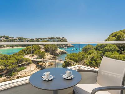 Balcony with table, two coffee cups, and sea view with trees and clear blue sky.