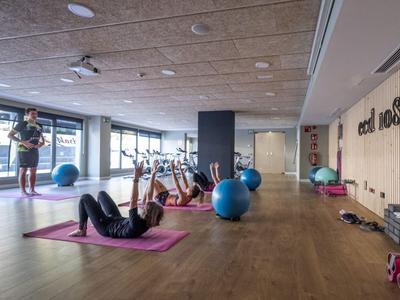 Innenraum eines Fitnessstudios mit Personen, die auf Yogamatten Übungen mit Hanteln und Gymnastikbällen machen.