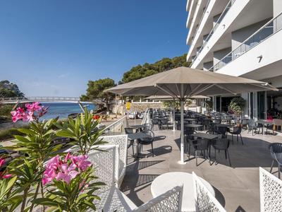 Outdoor terrace seating at a waterfront hotel with umbrellas and nearby pink flowers.
