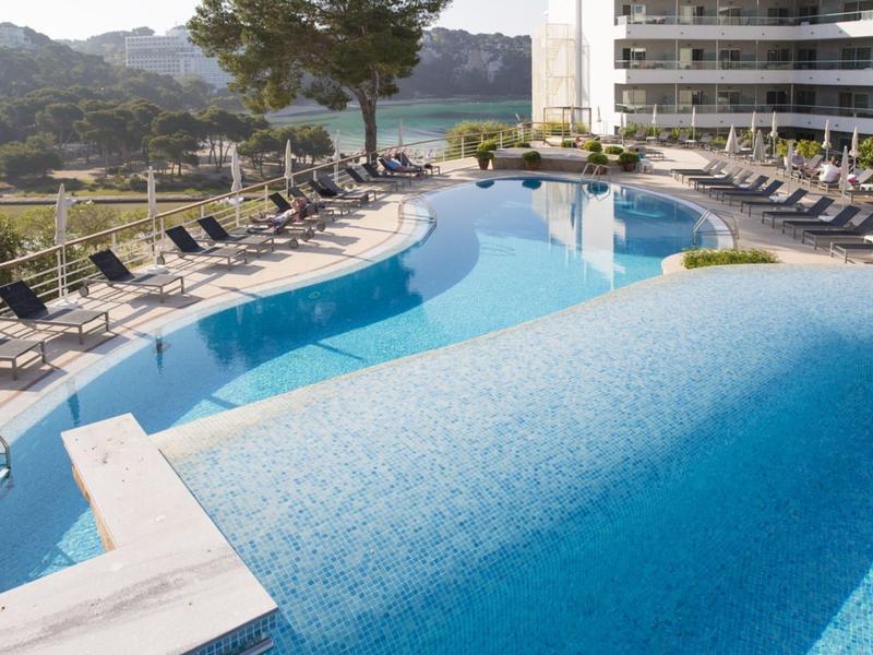 A luxurious hotel pool with sun loungers and mountain view in the background.