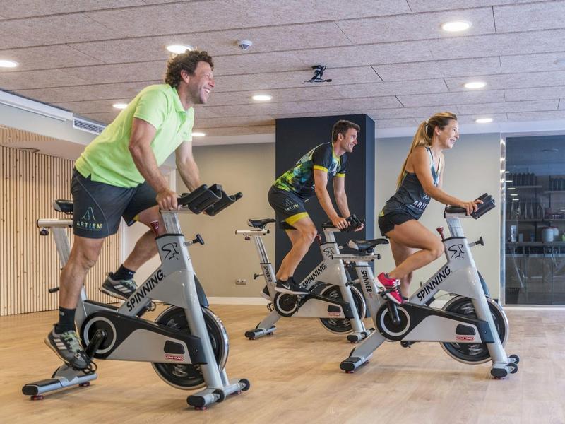 Three people exercising on stationary bikes in a modern gym with wooden walls and ceiling.