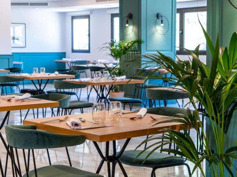 Modern hotel restaurant with wooden tables, blue chairs, and green indoor plants.