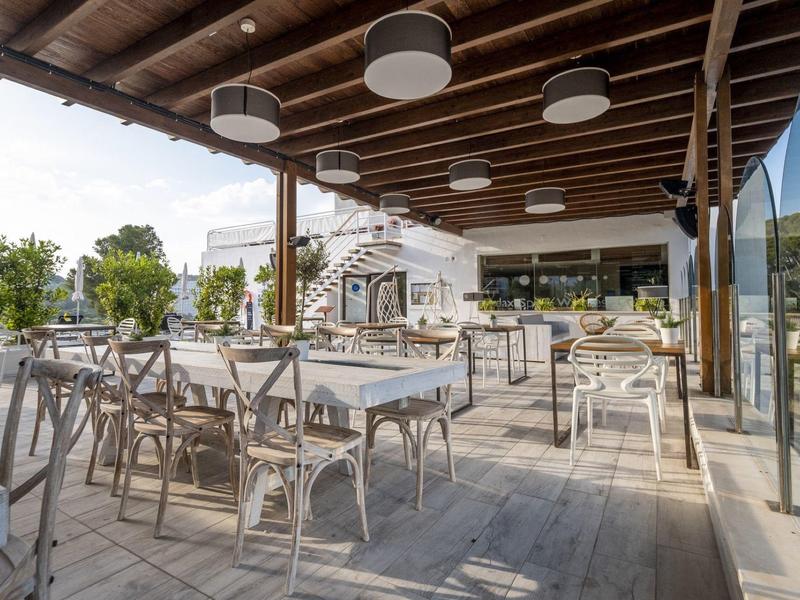 Spacious outdoor dining area with tables, chairs, and wooden ceiling under shaded roof.