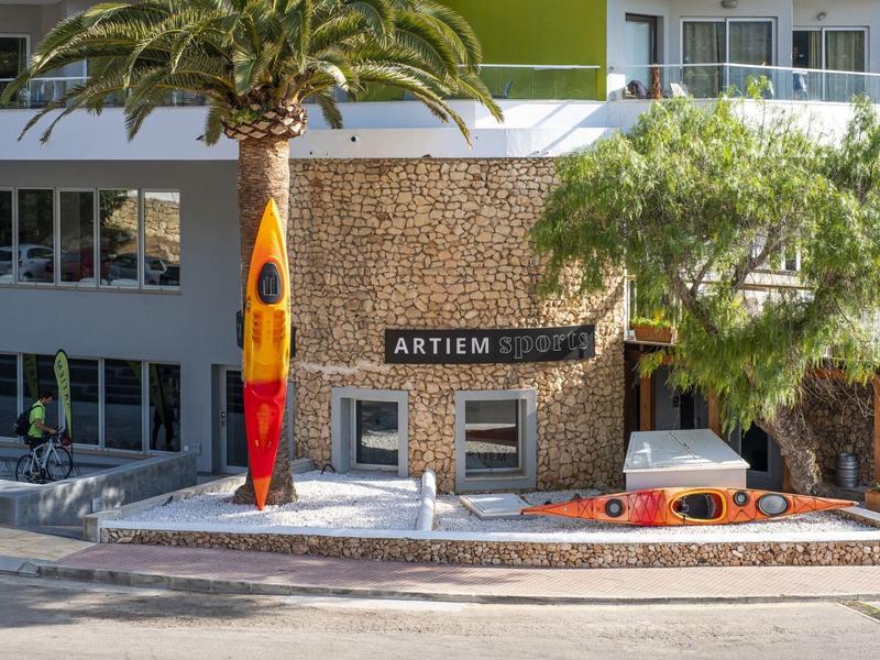 Hotel Artiem with palm trees and colorful surfboards outside its stone facade entrance.