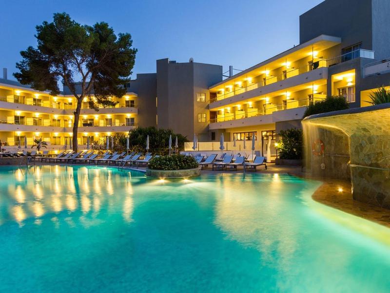 Hotel with illuminated balconies and large outdoor pool at dusk.