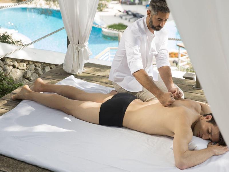 A man receives a back massage outdoors near a pool under a white canopy.