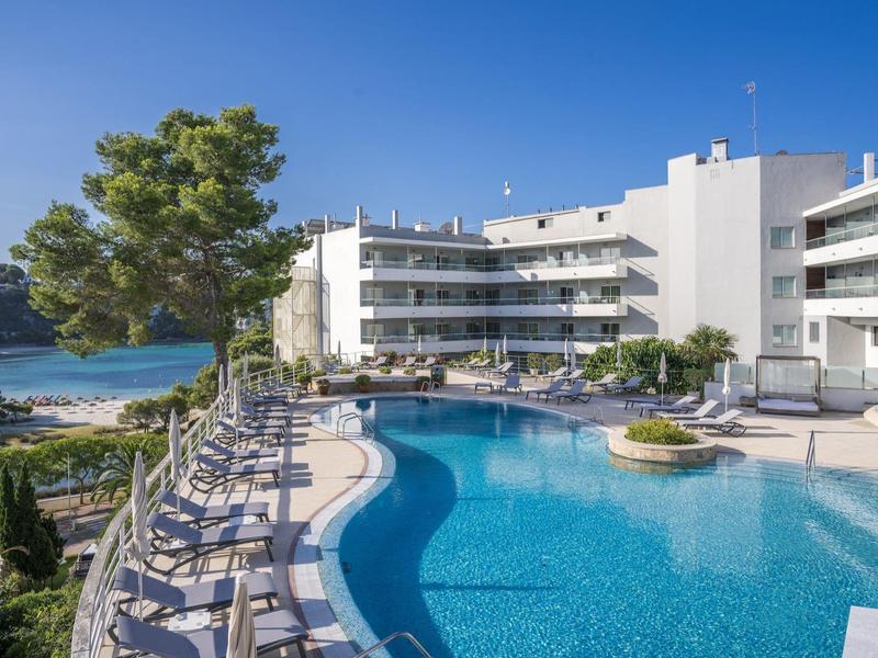 Resort hotel with curved pool, lounge chairs, near beach and greenery under clear sky.