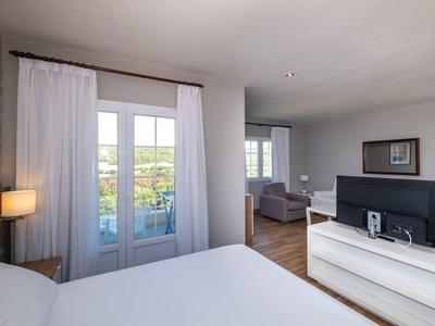 Chambre d'hôtel lumineuse avec lit double, télévision sur commode et terrasse donnant sur la verdure.