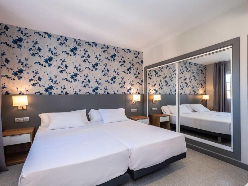 Chambre d'hôtel moderne avec lit double, mur d'accent floral et grand miroir.