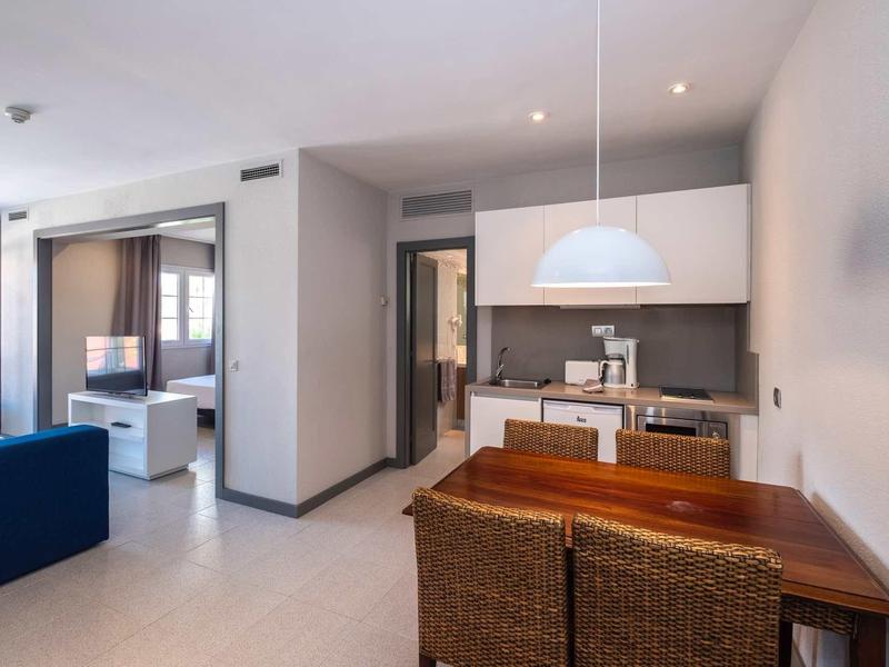 Coin repas moderne avec table en bois et chaises en osier à côté d'une cuisine ouverte dans un appartement lumineux.
