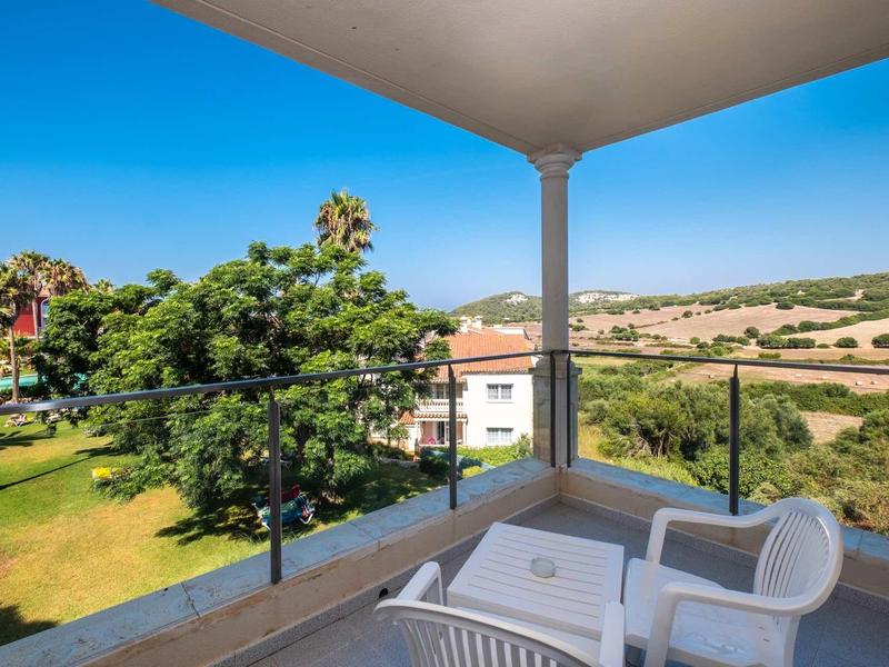 Balcon avec deux fauteuils et une table donnant sur des arbres et des champs sous un ciel bleu.