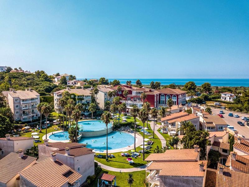 Complexe hôtelier avec piscine, palmiers et vue sur la mer sous un ciel dégagé.
