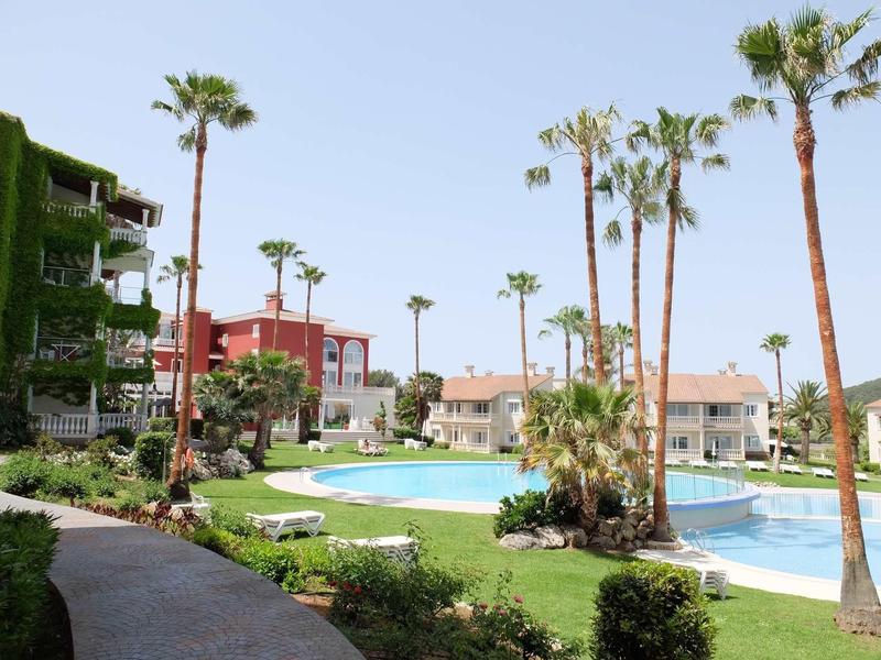 Grand piscine avec palmiers et transats dans un complexe hôtelier sous ciel dégagé.