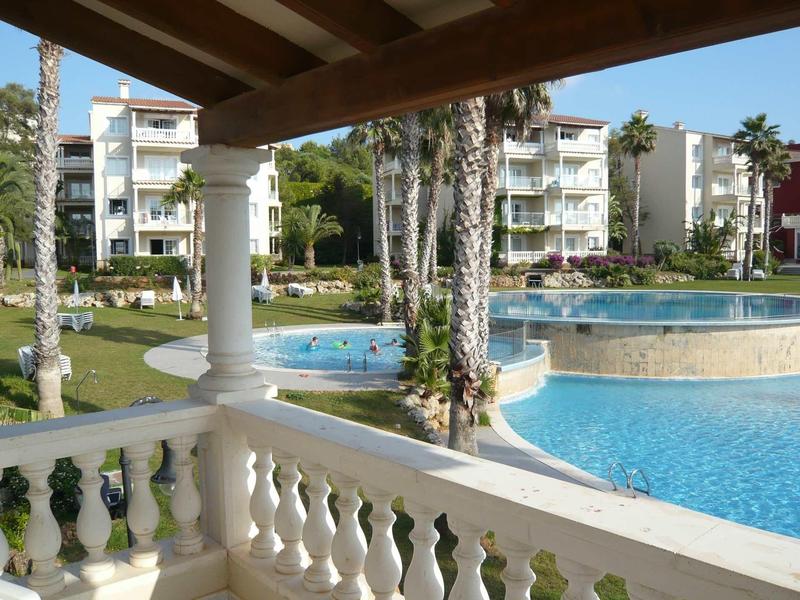 Balcon avec colonnes blanches donnant sur une piscine et des bâtiments d'hôtel dans un cadre tropical.