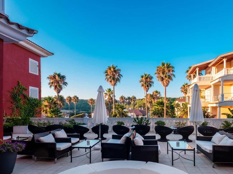 Terrasse avec sièges modernes, parasols et palmiers sous un ciel bleu clair.