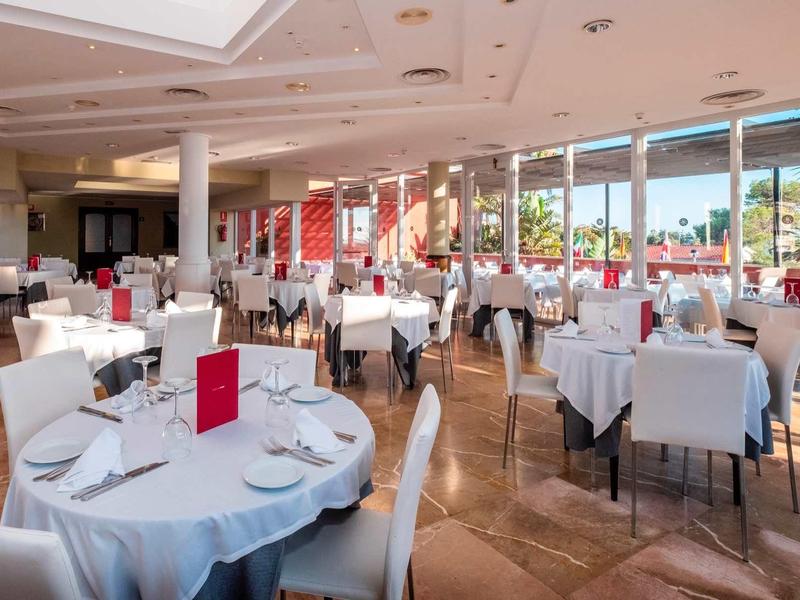 Restaurant élégant avec nappes blanches et grandes fenêtres donnant sur des palmiers.