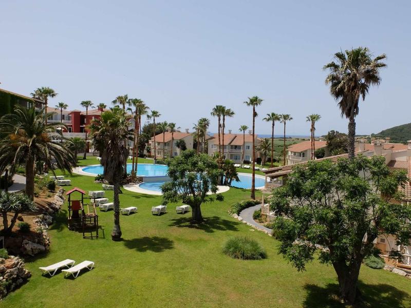 Jardin d'hôtel avec plusieurs piscines, palmiers et chaises longues sous un ciel bleu
