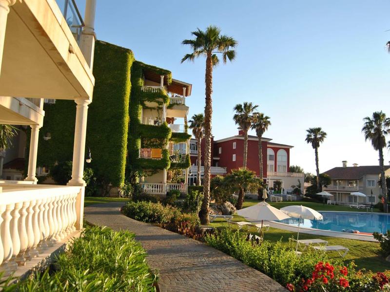 Complexe hôtelier avec piscine, palmiers et chemin entre les bâtiments sous un ciel clair.