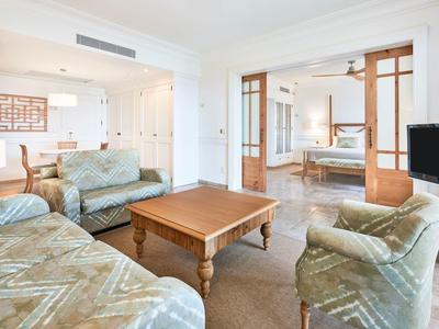 Helles Wohnzimmer mit grünen Sofas, Holztisch, Fernseher und Blick ins Ess- und Schlafzimmer.