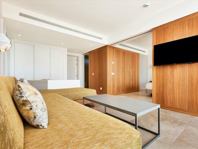Modern hotel room with brown sofa, wooden walls, and large wall-mounted TV.