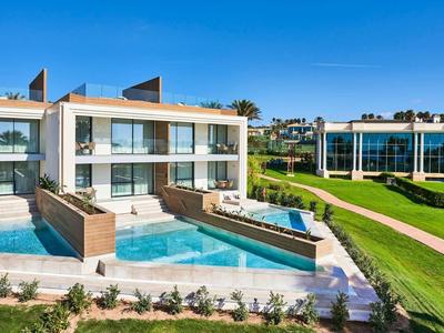 Modern holiday complex with pool, terrace, and green lawns under a blue sky.