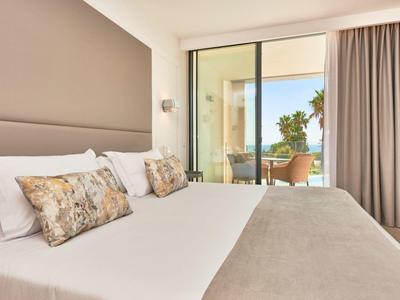 Modern hotel room with large bed, balcony, and palm tree view