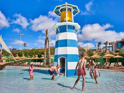 Children playing in a shallow pool with a blue and white lighthouse play structure.