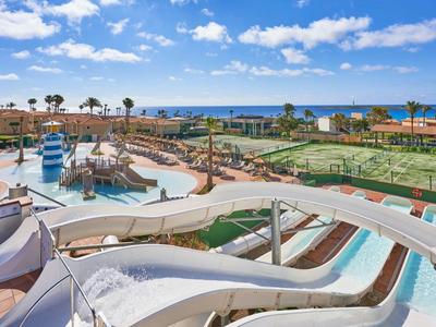 Waterpark with water slides, pool, tennis courts, and sea view on a sunny day.