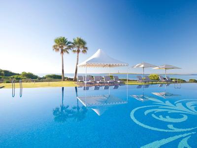 Infinity-Pool mit Liegestühlen und Sonnenschirmen, Palmen im Hintergrund und Meerblick