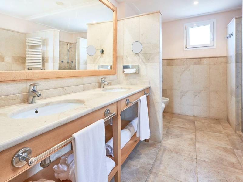 Spacious bathroom with double sinks, large mirrors, and beige tiles.
