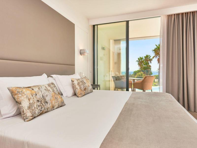 Modern hotel room with large bed, balcony, and palm tree view