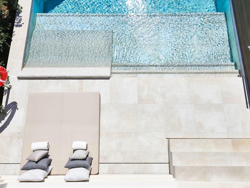 Two lounge chairs with cushions beside a pool with clear water and steps.