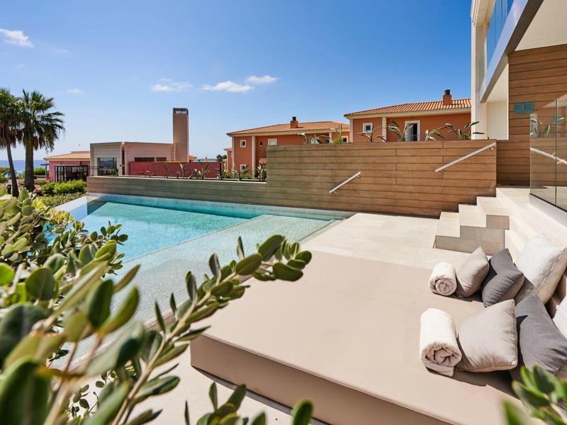 Luxurious pool terrace with sun loungers, towels, and palm trees under a blue sky.