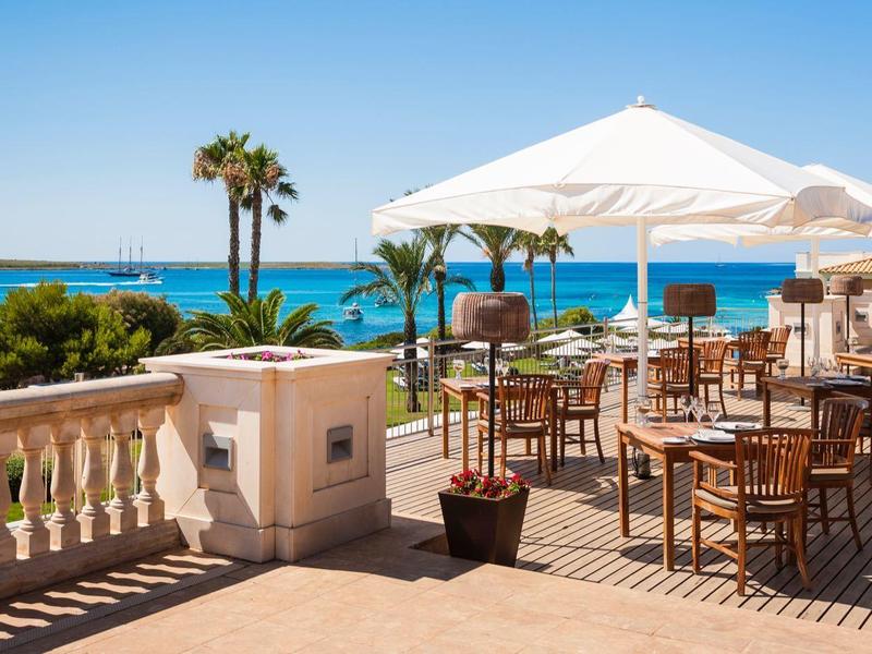 Large hotel terrace with tables, chairs, umbrellas overlooking the sea and palm trees.